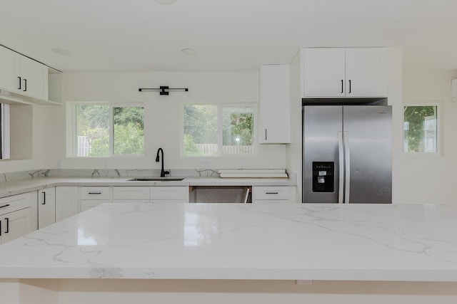 kitchen featuring light stone counters, sink, white cabinetry, plenty of natural light, and stainless steel fridge