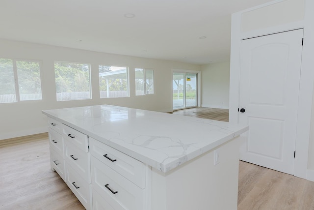 kitchen featuring a kitchen island, light stone counters, light hardwood / wood-style floors, and white cabinetry