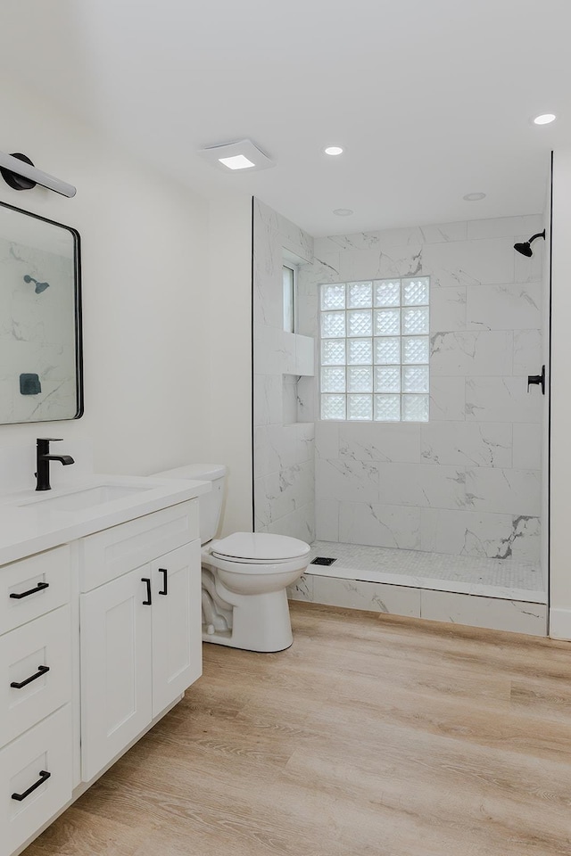 bathroom featuring tiled shower, vanity, hardwood / wood-style flooring, and toilet