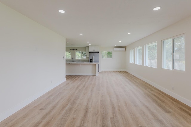 unfurnished living room featuring sink, light hardwood / wood-style flooring, and a wall mounted AC