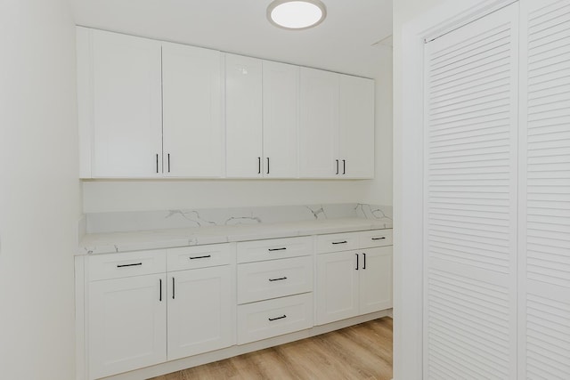 kitchen with white cabinets, light hardwood / wood-style flooring, and light stone countertops