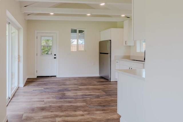 kitchen with sink, white cabinets, stainless steel fridge, beamed ceiling, and hardwood / wood-style floors