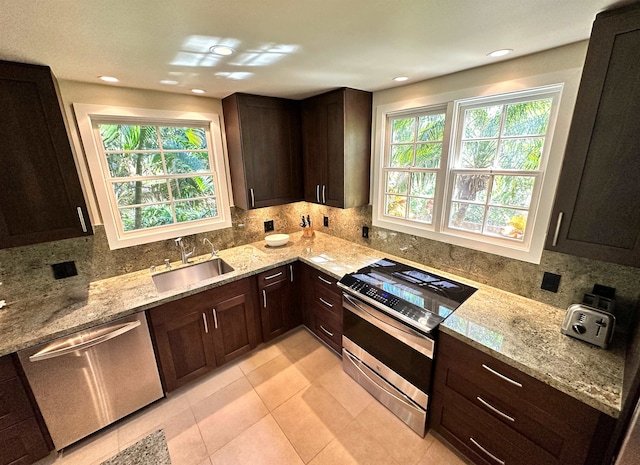 kitchen with appliances with stainless steel finishes, light stone counters, light tile floors, sink, and dark brown cabinetry