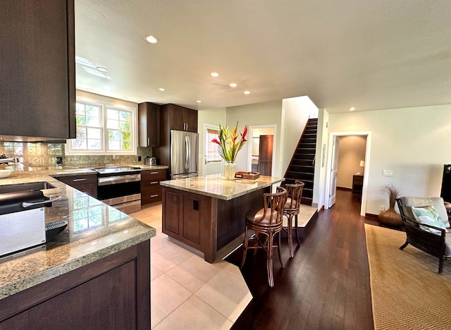 kitchen with appliances with stainless steel finishes, a kitchen island, light hardwood / wood-style floors, dark brown cabinets, and light stone countertops