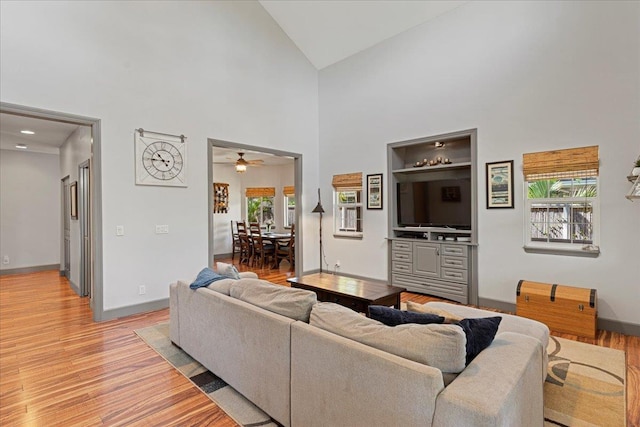 living room with light wood-type flooring, high vaulted ceiling, and ceiling fan