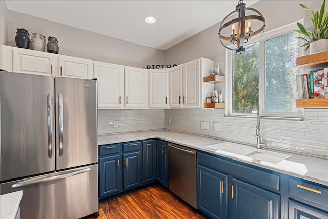 kitchen featuring white cabinets, blue cabinetry, appliances with stainless steel finishes, a notable chandelier, and light stone counters