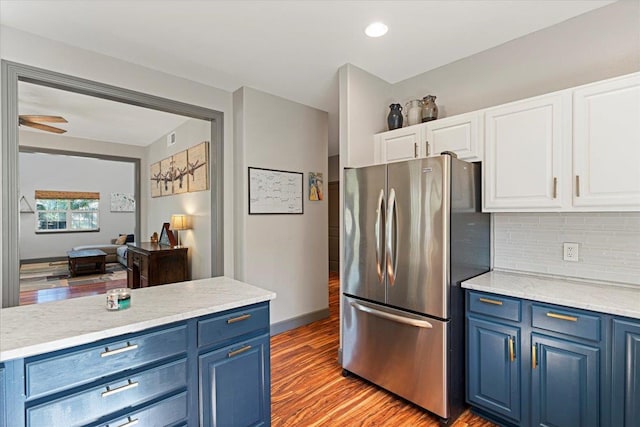 kitchen with blue cabinets, light hardwood / wood-style flooring, tasteful backsplash, white cabinetry, and stainless steel refrigerator