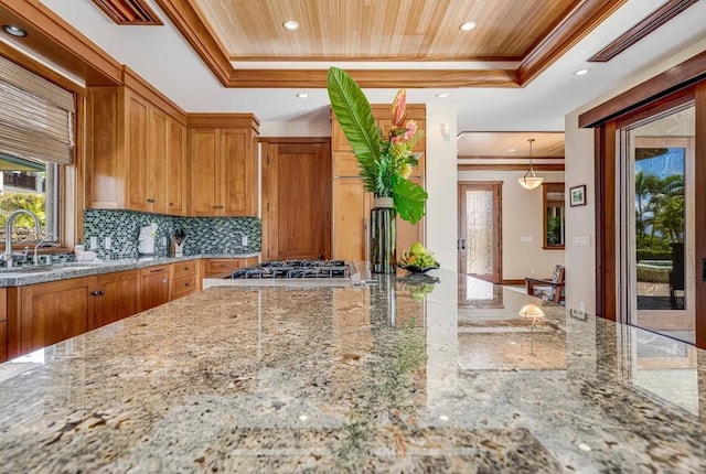 kitchen featuring backsplash, sink, light stone counters, a raised ceiling, and pendant lighting