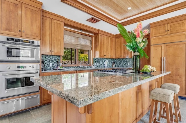 kitchen featuring backsplash, light stone counters, a breakfast bar area, a center island, and stainless steel appliances