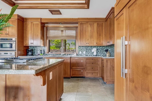 kitchen with built in refrigerator, decorative backsplash, sink, and light stone counters