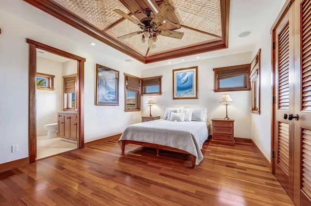 bedroom with a tray ceiling, ceiling fan, hardwood / wood-style flooring, and ensuite bathroom