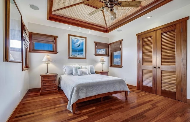 bedroom with ceiling fan, a raised ceiling, french doors, and wood-type flooring