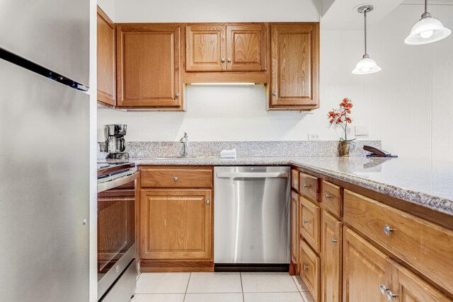 kitchen with appliances with stainless steel finishes, light stone counters, sink, light tile patterned floors, and decorative light fixtures