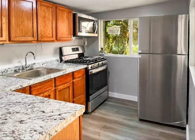 kitchen featuring brown cabinetry, light stone countertops, a sink, stainless steel appliances, and light wood-style floors