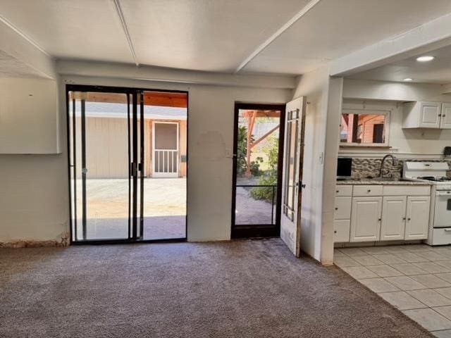 kitchen with light tile patterned flooring, a sink, white cabinets, white gas range oven, and light colored carpet