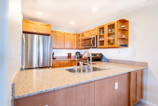 kitchen with stainless steel appliances, a peninsula, a sink, light stone countertops, and glass insert cabinets