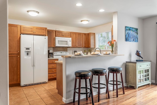 kitchen featuring sink, white appliances, a kitchen breakfast bar, and kitchen peninsula