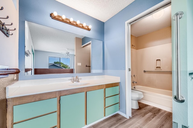 full bath with toilet, wood finished floors, a textured ceiling, vanity, and washtub / shower combination