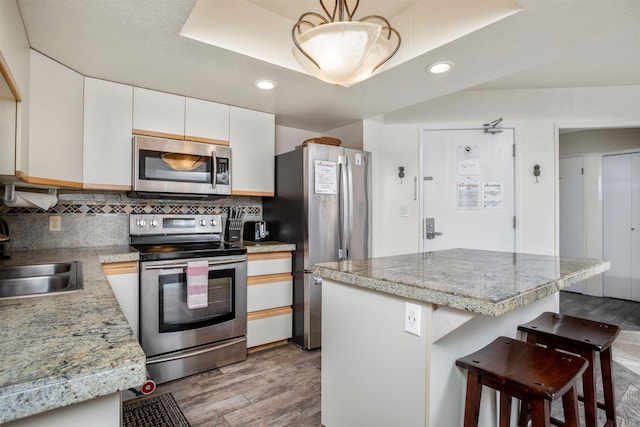 kitchen featuring sink, a kitchen island, a breakfast bar, white cabinets, and appliances with stainless steel finishes