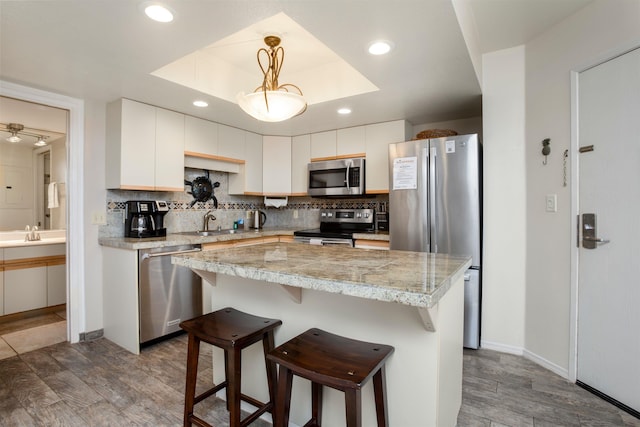 kitchen with a tray ceiling, white cabinets, pendant lighting, and appliances with stainless steel finishes