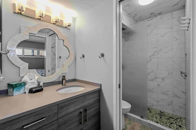 bathroom with a textured wall, a tile shower, vanity, and toilet