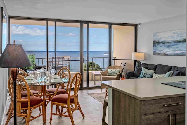 dining space with a wall of windows, a water view, and light wood finished floors