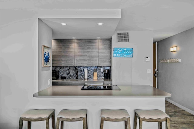 kitchen with black electric cooktop, a breakfast bar, a sink, visible vents, and dark wood-style floors