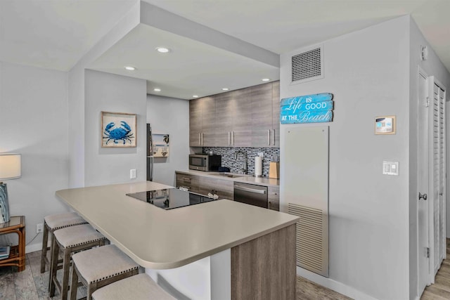 kitchen with backsplash, a kitchen breakfast bar, appliances with stainless steel finishes, light hardwood / wood-style floors, and kitchen peninsula