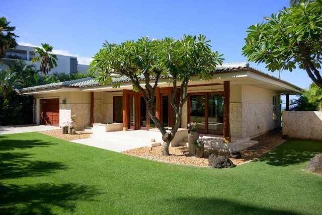 rear view of house with an attached garage, stucco siding, stone siding, a tile roof, and a lawn