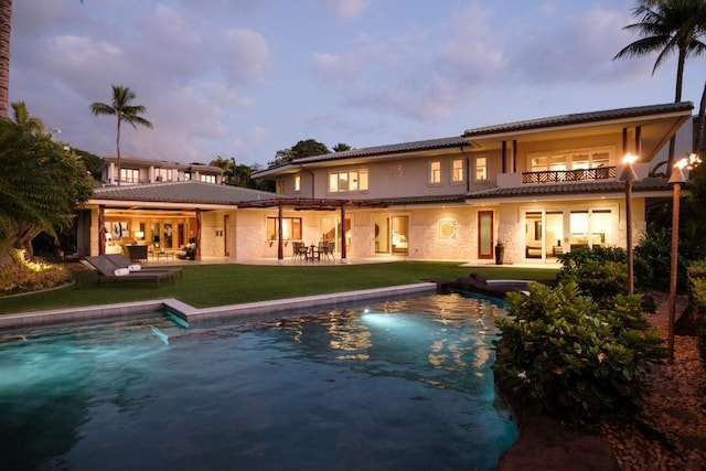 rear view of house featuring stucco siding, a yard, an outdoor pool, a balcony, and a patio area