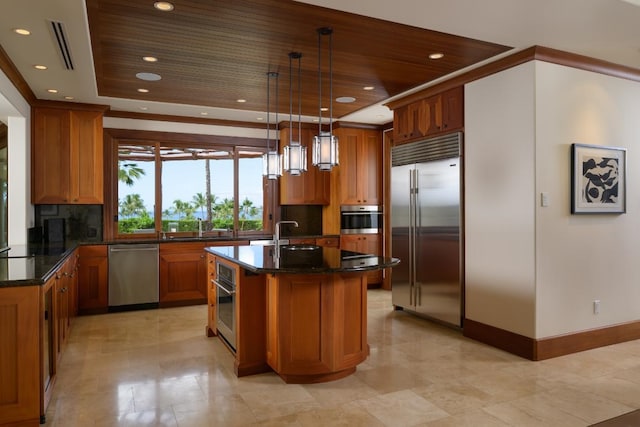 kitchen with a tray ceiling, dark stone counters, stainless steel appliances, decorative backsplash, and brown cabinets