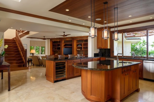 kitchen featuring beverage cooler, dark stone counters, stainless steel dishwasher, brown cabinetry, and a kitchen island with sink