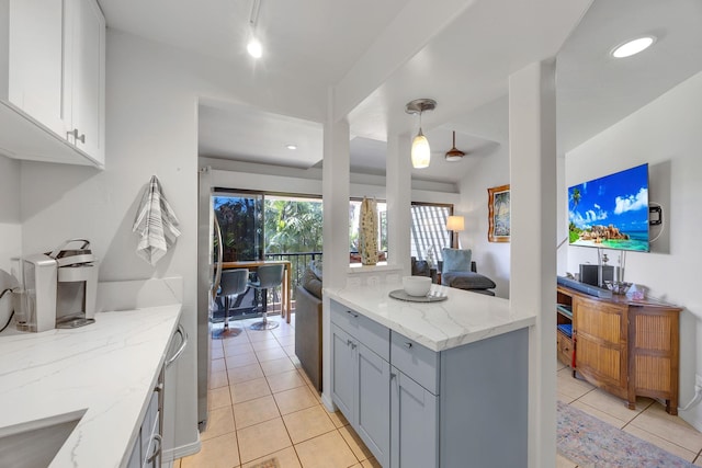 kitchen featuring gray cabinetry, light stone counters, hanging light fixtures, light tile patterned floors, and white cabinets