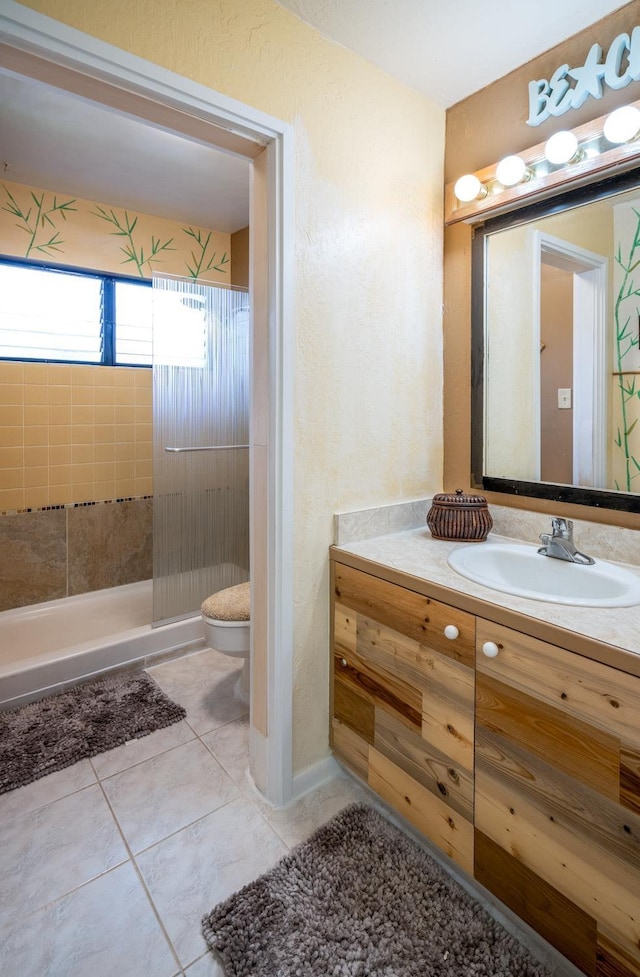 bathroom with tile patterned flooring, vanity, a tile shower, and toilet