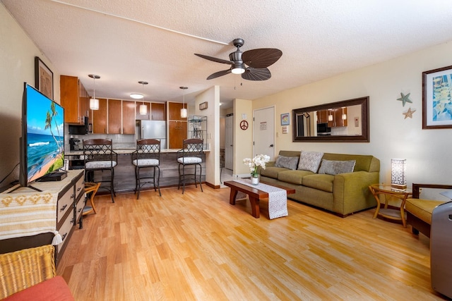 living room with ceiling fan, a textured ceiling, and light wood-type flooring