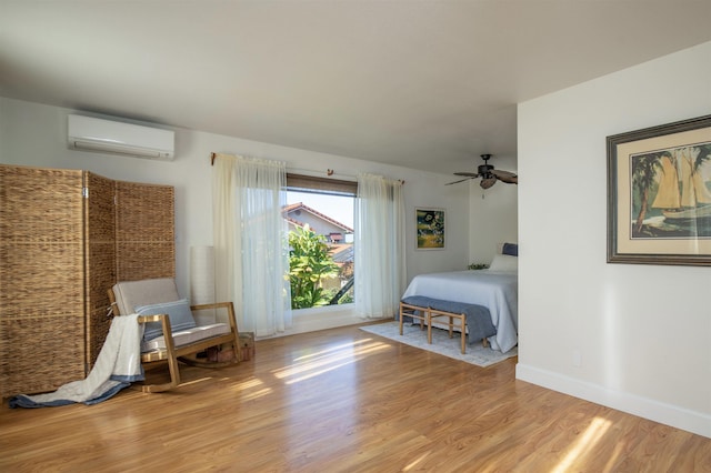 bedroom featuring a wall mounted AC, light hardwood / wood-style flooring, and ceiling fan