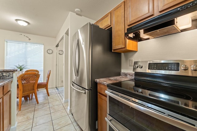 480 Kenolio Rd Unit 21-101, Kihei, HI 96753 - kitchen featuring range with two ovens, under cabinet range hood, brown cabinetry, light tile patterned floors, and baseboards