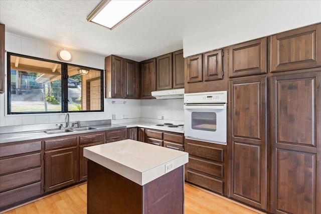 kitchen featuring light wood-type flooring, a textured ceiling, white appliances, sink, and a center island