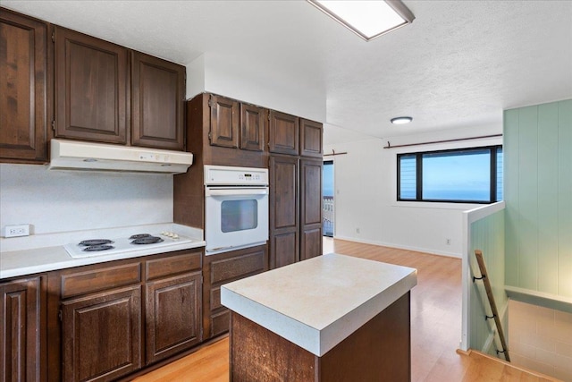 kitchen with dark brown cabinetry, a center island, white appliances, and light wood-type flooring