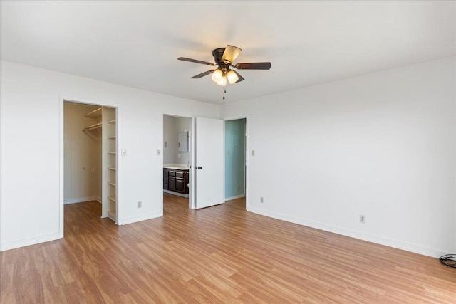 unfurnished bedroom with a walk in closet, ceiling fan, light wood-type flooring, connected bathroom, and a closet