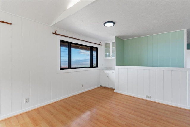 spare room with wooden walls, light hardwood / wood-style flooring, and a textured ceiling