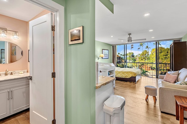 bedroom with floor to ceiling windows, sink, ensuite bathroom, and light hardwood / wood-style floors