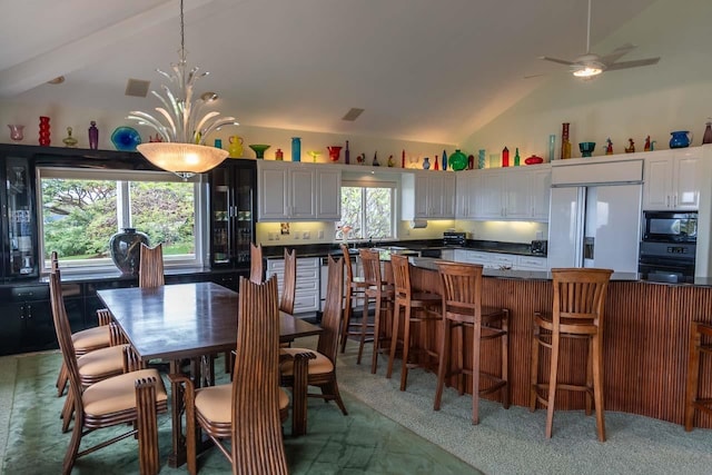 carpeted dining area with ceiling fan with notable chandelier and vaulted ceiling