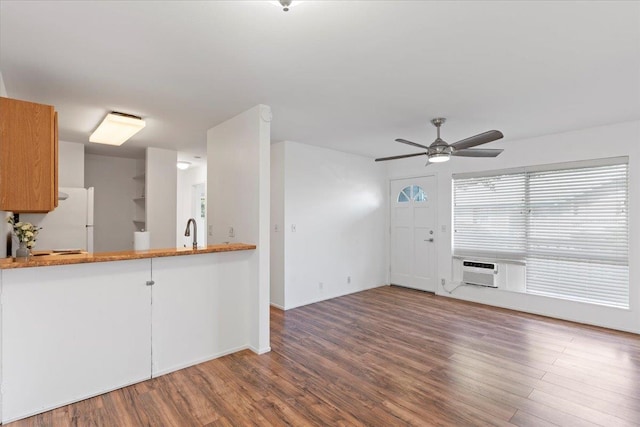 unfurnished living room with wood-type flooring, a wall unit AC, ceiling fan, and sink