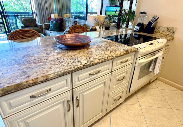 kitchen with light stone counters, electric range, a wealth of natural light, and light tile flooring