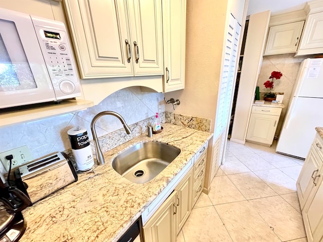 kitchen with tasteful backsplash, light tile floors, light stone countertops, white appliances, and sink