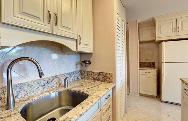 kitchen featuring white fridge, sink, tasteful backsplash, and light stone counters