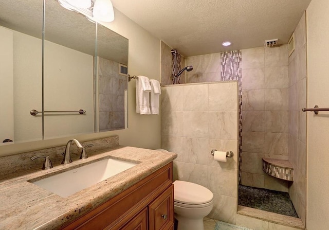 bathroom with tile walls, toilet, a tile shower, a textured ceiling, and vanity