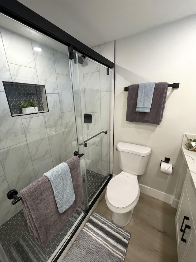 bathroom featuring wood finished floors, toilet, a marble finish shower, and baseboards