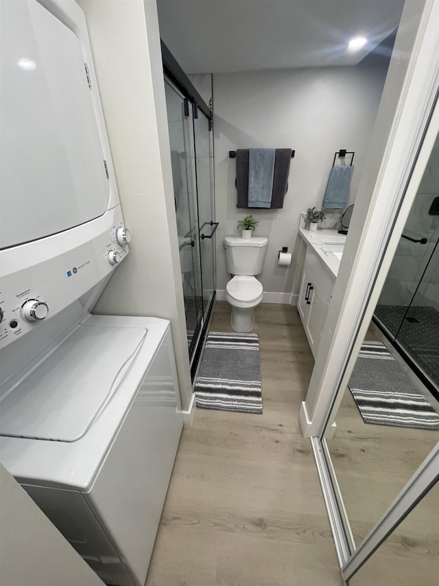 bathroom featuring stacked washing maching and dryer, vanity, toilet, a stall shower, and wood finished floors